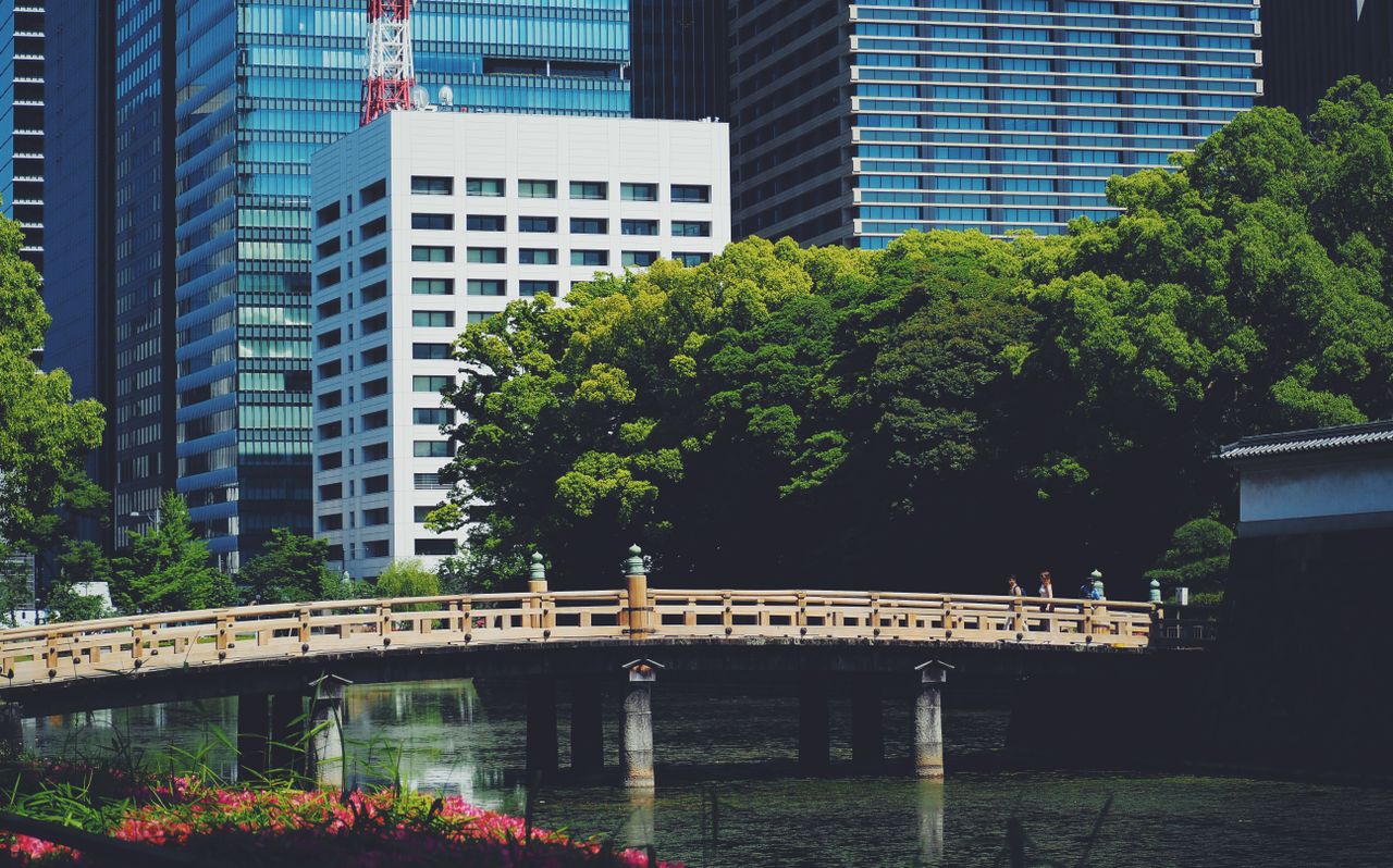 A scenic view of Tokyo with skyscrapers and a traditional bridge over a reflective pond.